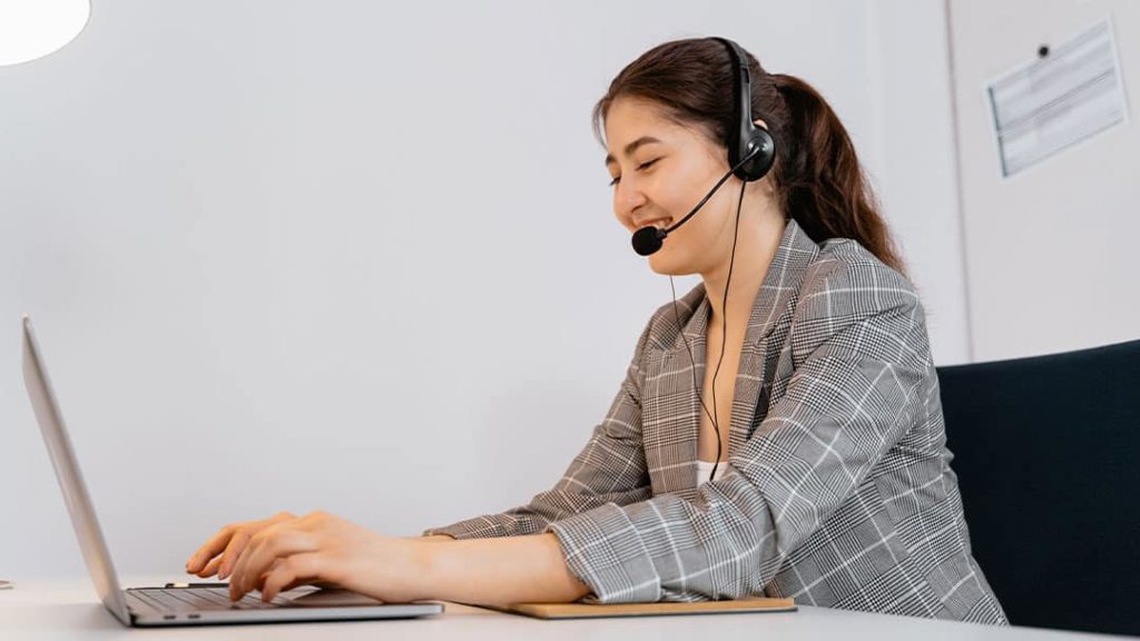 A smiling female remote telemarketing professional making a call from a office room